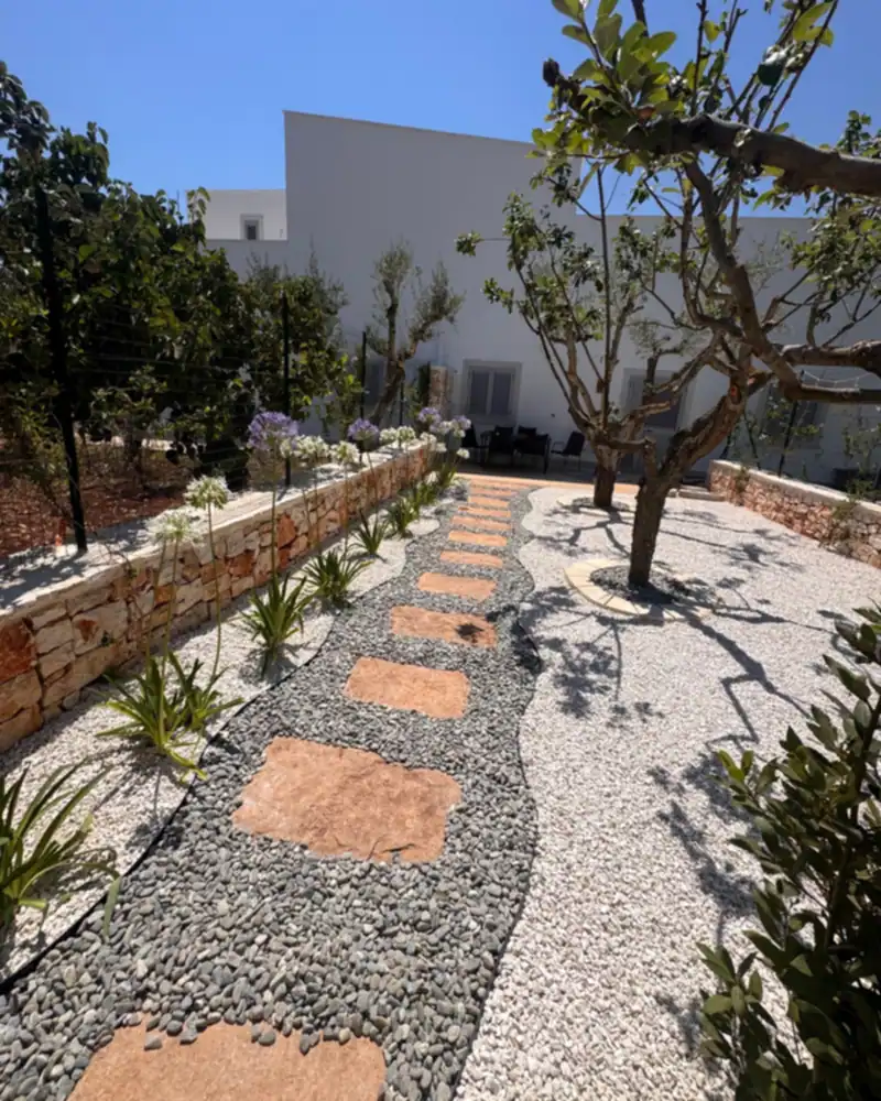 Sentiero in pietra e ghiaia tra agrumi e aiuole mediterranee in un giardino realizzato da Cesarino Giardini