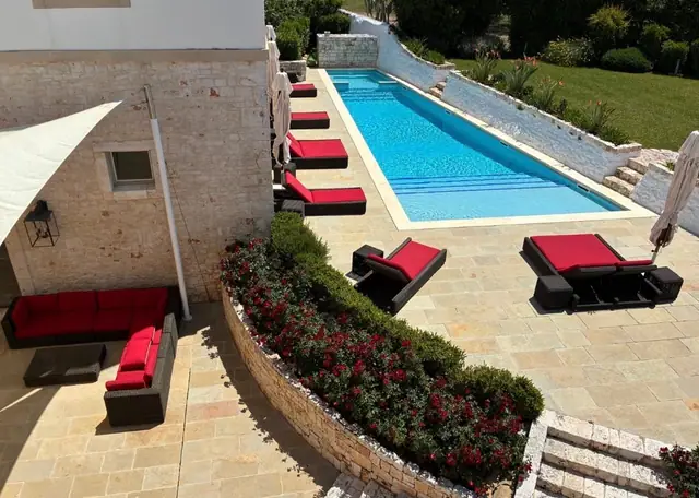 Piscina di una villa in pietra con aiuole fiorite di rosso